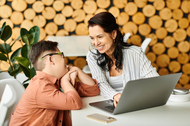 adorable inclusivo chico con síndrome de Down pasar tiempo con su alegre madre delante de la computadora portátil - Foto, Imagen