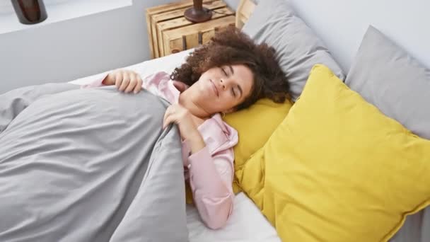 Egy fiatal spanyol nő göndör hajjal ellazul fényes hálószobájában, bemutatva a kikapcsolódást és a kényelmet. - Felvétel, videó