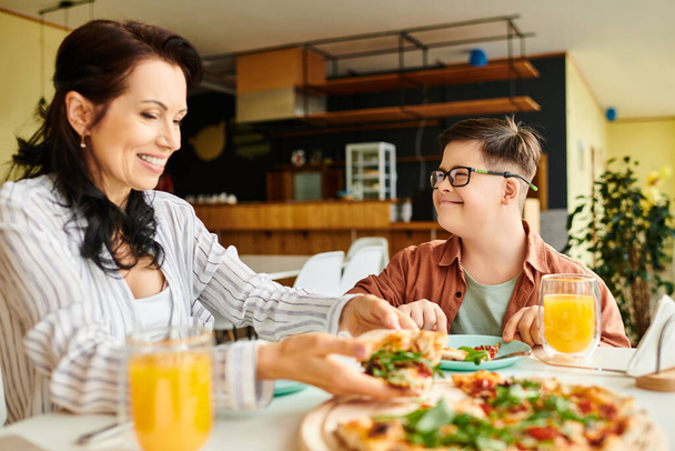 allegra madre mangiare pizza e bere succo di frutta con il suo figlio carino inclusivo con la sindrome di Down - Foto, immagini
