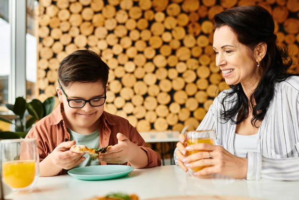 Fröhliche Mutter isst Pizza und trinkt Saft mit ihrem netten Sohn mit Down-Syndrom - Foto, Bild