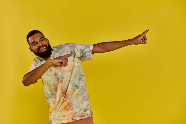 Een man met een levendig stropdas kleurstof shirt wijst levendig naar iets buiten beeld, zijn kleurrijke kledij die opvalt tegen een neutrale achtergrond. - Foto, afbeelding