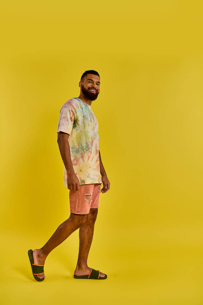 Ένας άντρας που φοράει ένα πολύχρωμο μπλουζάκι και ασορτί σορτς στέκεται με αυτοπεποίθηση, αναδεικνύοντας το μοναδικό και ζωντανό στυλ του σε ένα χαλαρό περιβάλλον. - Φωτογραφία, εικόνα