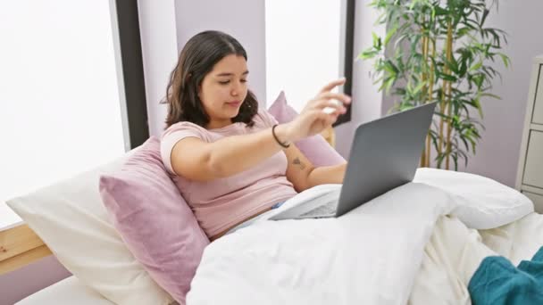 Junge hispanische Frau schließt Laptop in ihrem Schlafzimmer mit Pflanze im Hintergrund und verkörpert Entspannung und digitale Entgiftung. - Filmmaterial, Video