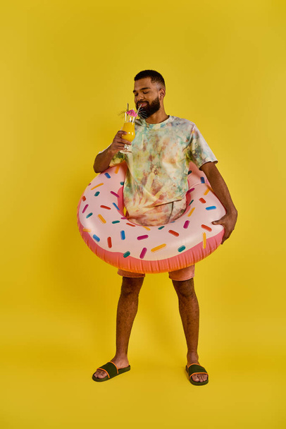 Ein Mann im pulsierenden Krawattenhemd hält fröhlich ein erfrischendes Getränk in der einen Hand und einen lustigen Donut in der anderen.. - Foto, Bild