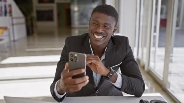 現代のオフィスの設定でスマートフォンを使用するアフリカ系アメリカ人ビジネスマン - 映像、動画