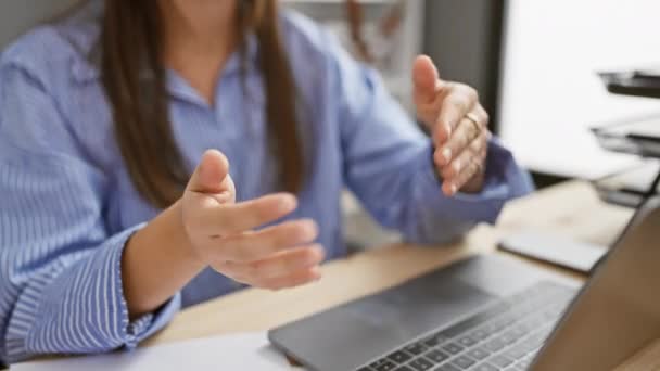 Una giovane donna ispanica in camicia a righe gesti durante una riunione alla scrivania del suo ufficio, mostrando interazione e comunicazione. - Filmati, video