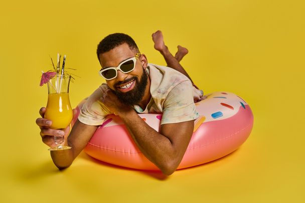 Een man zit ontspannen op een opblaasbare praalwagen op het water, met een drankje in zijn hand terwijl hij geniet van een moment van ontspanning. - Foto, afbeelding