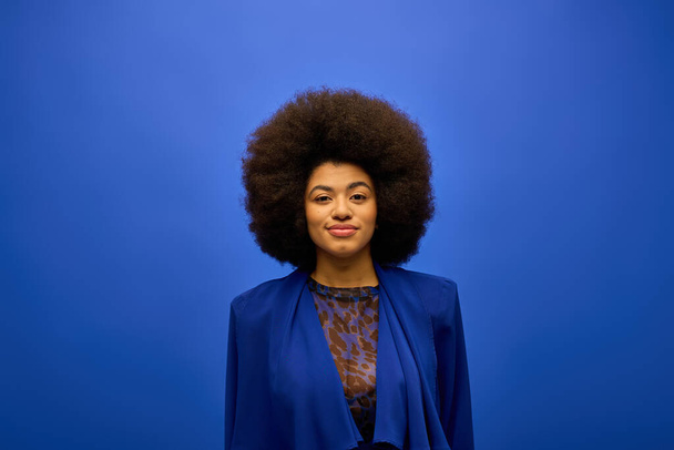 Stijlvolle Afro-Amerikaanse vrouw met krullend haar staat vol vertrouwen tegen een levendige blauwe achtergrond. - Foto, afbeelding