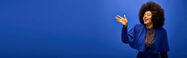 Stylová Afroameričanka s kudrnatým účesem stojí sebevědomě na pulzujícím modrém pozadí. - Fotografie, Obrázek