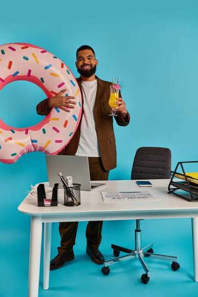Um homem com uma expressão alegre segura um donut enorme e delicioso em uma mão enquanto equilibra uma bebida refrescante na outra.. - Foto, Imagem