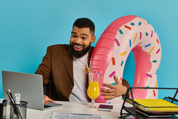 Ένας άνθρωπος σε μια στοχαστική στάση, κάθεται σε ένα γραφείο με ένα φορητό υπολογιστή ανοιχτό μπροστά του και ένα ποτό στο πλευρό του. - Φωτογραφία, εικόνα