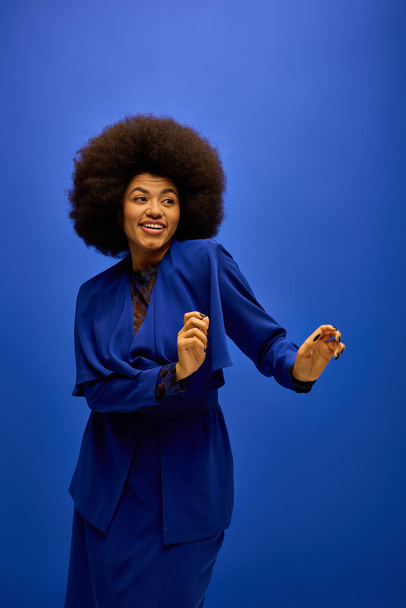 Κομψό Αφροαμερικανή γυναίκα σε μπλε κοστούμι με σγουρά μαλλιά ποζάρουν σε ένα ζωντανό σκηνικό. - Φωτογραφία, εικόνα