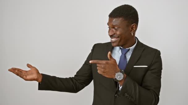 Даппер афроамериканец в деловом костюме, удивленный тем, как он улыбается и указывает, уверенно стоя, показывая рукой на изолированном белом фоне - Кадры, видео