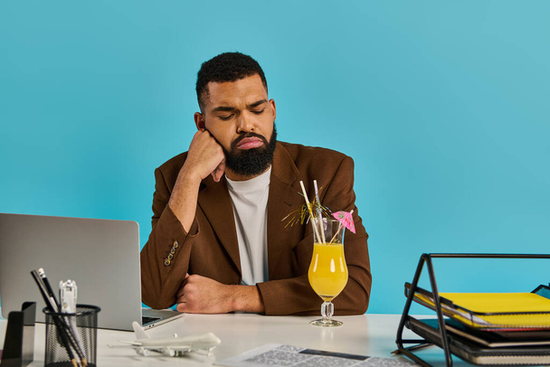 Ένας άντρας κάθεται σε ένα γραφείο, έντονα συγκεντρωμένος στην οθόνη του λάπτοπ του, με ένα δροσιστικό ποτό δίπλα του.. - Φωτογραφία, εικόνα