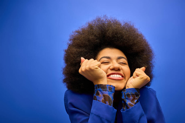 Tyylikäs afroamerikkalainen nainen, jolla on kiharat hiuskilometrit ja joka pitää käsiään kasvojensa edessä iloisessa asennossa. - Valokuva, kuva