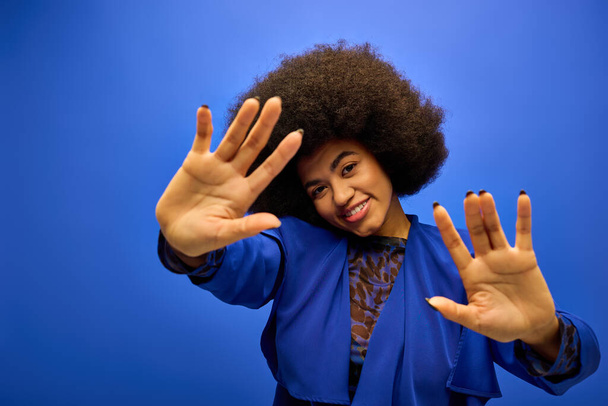 Elegante mujer afroamericana con el pelo rizado en traje de moda, levantando alegremente sus manos. - Foto, Imagen