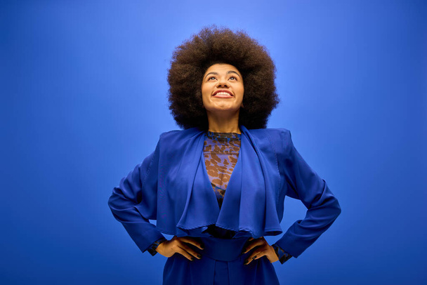 Afroamerykanka z kręconymi włosami stylowo na tętniącym życiem niebieskim tle. - Zdjęcie, obraz