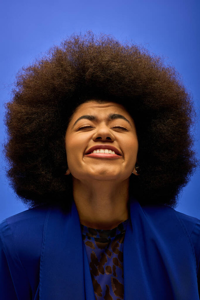 Stijlvolle Afro-Amerikaanse vrouw met krullend haarhaar glimlachend in een blauwe jas. - Foto, afbeelding