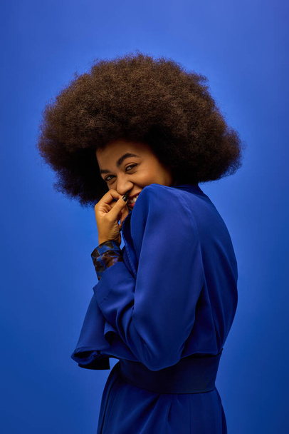 明るい青い背景の前に曲がったヘアードロップを持つファッショナブルなアフリカ系アメリカ人女性. - 写真・画像