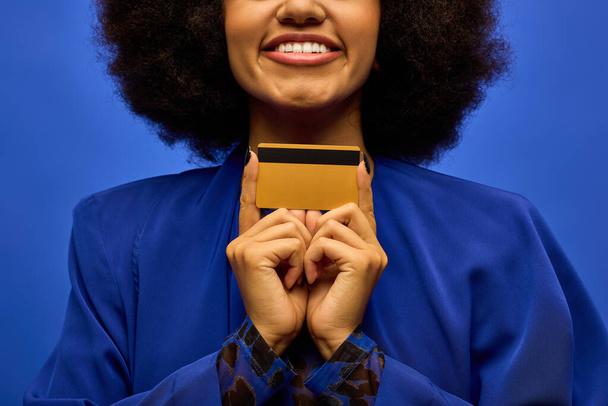 彼女の顔にクレジットカードを保持するトレンディな服装でスタイリッシュなアフリカ系アメリカ人女性. - 写真・画像