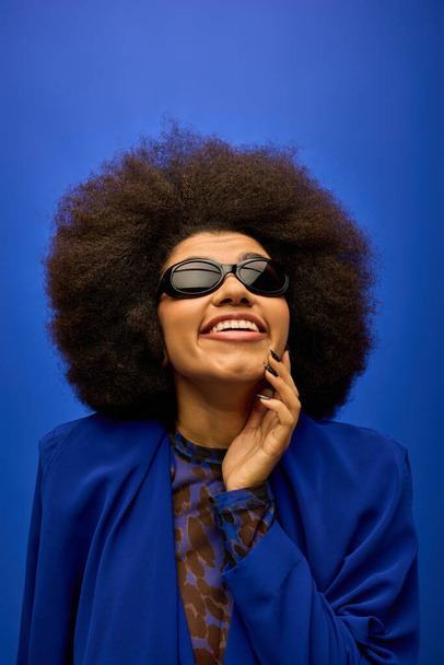 Trendy Afro-Amerikaanse vrouw poseert in blauwe jas en zonnebril. - Foto, afbeelding
