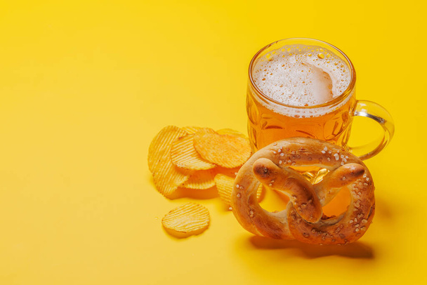 Пиво, чипсы и крендель. На жёлтом фоне с копировальным пространством - Фото, изображение