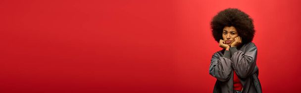 Стильна афроамериканська жінка з кучерявим віялом впевнено на яскраво-червоному тлі. - Фото, зображення