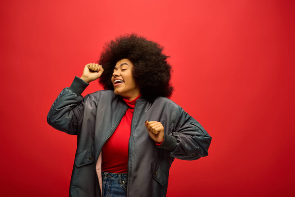 Stylish African American woman with curly hairdoposing in front of a vibrant red backdrop. - Photo, Image