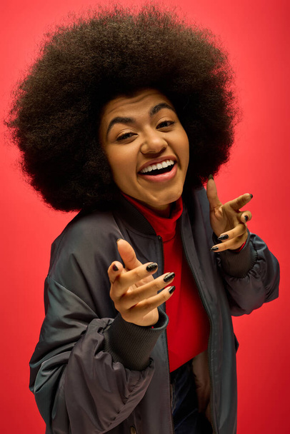 Eine stylische Afroamerikanerin mit lockigem Haar, die vor einer lebendigen Kulisse ein lustiges Gesicht zeigt. - Foto, Bild