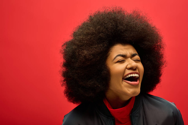 Stylish African American woman with curly hairdohair on a vibrant red backdrop. - Photo, Image