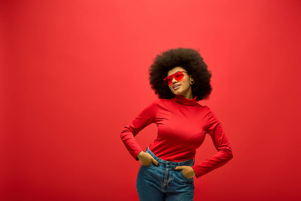 Stijlvolle Afro-Amerikaanse vrouw draagt een rood shirt met een rood hart op haar gezicht poseert tegen een levendige achtergrond. - Foto, afbeelding