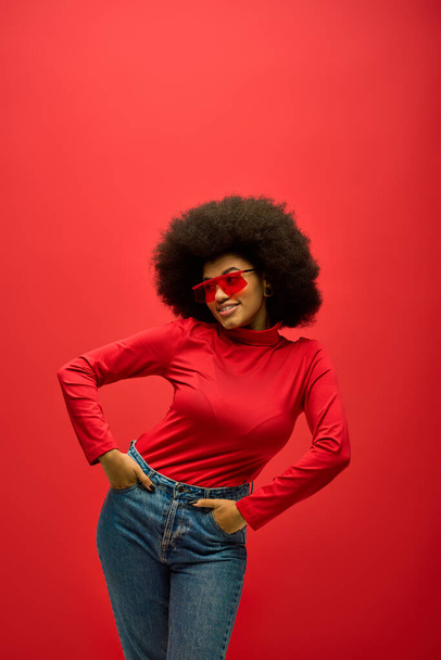 Elegante mujer afroamericana con gafas de sol rojas en la cara, posando sobre un vibrante telón de fondo. - Foto, Imagen