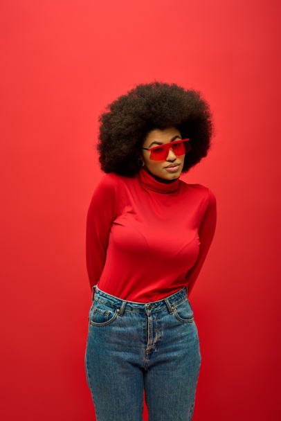 アフリカ系アメリカ人女性,トレンディな赤シャツと活気に満ちた背景にジーンズをポーズ. - 写真・画像