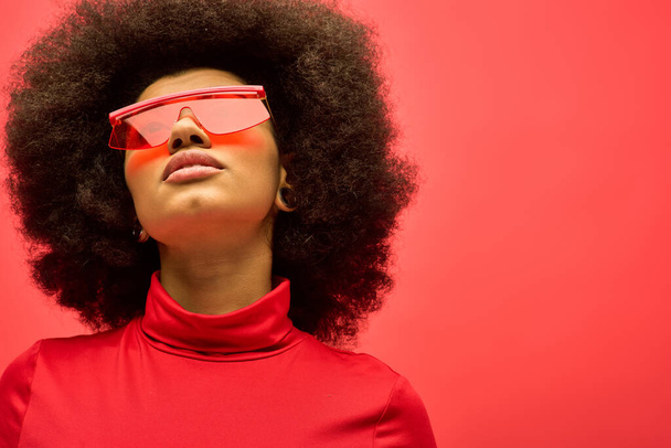 Μια μοντέρνα Αφροαμερικανή ποζάρει με κόκκινα γυαλιά και πουκάμισο σε ένα ζωντανό σκηνικό. - Φωτογραφία, εικόνα