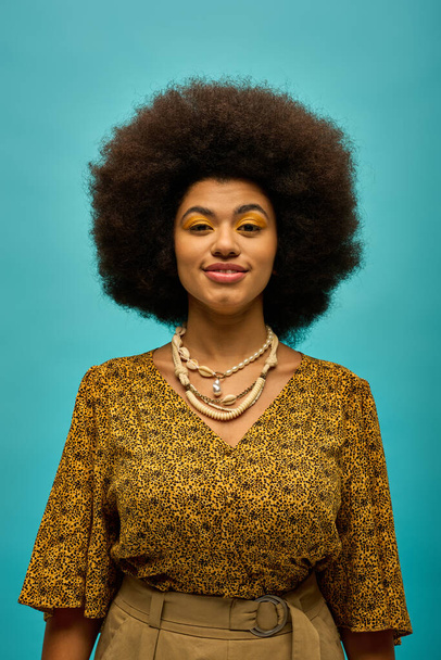 Trendige Afro-Amerikanerin mit Afro-Frisur posiert stilvoll vor leuchtend blauem Hintergrund. - Foto, Bild