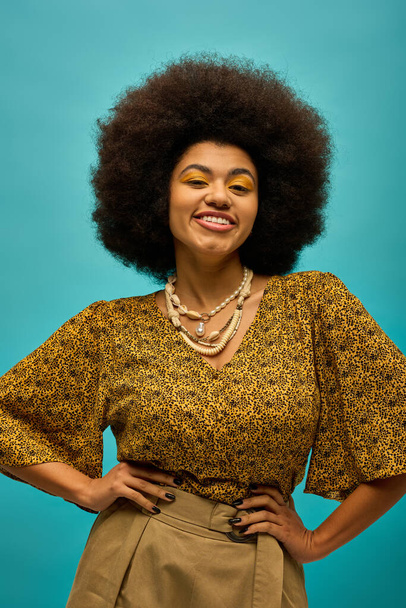 Модна афроамериканська жінка з кучерявим волоссям робить позу в стильному вбранні на яскраво-синьому фоні. - Фото, зображення