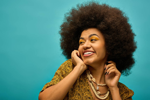Femme afro-américaine élégante avec des cheveux bouclés souriant pour la caméra en tenue tendance. - Photo, image