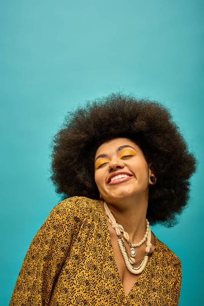 Een stijlvolle Afro-Amerikaanse vrouw met krullend kapsel glimlachend op een levendige achtergrond. - Foto, afbeelding