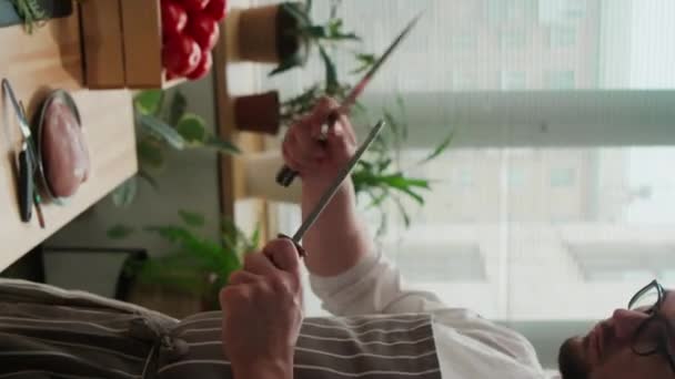 Colpo medio verticale dello chef maschio caucasico usando musato mentre affila il coltello da cucina prima di iniziare la cottura - Filmati, video