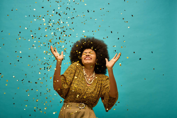 Een stijlvolle Afro-Amerikaanse vrouw met handen opgeheven in viering, confetti vallen uit haar haar. - Foto, afbeelding