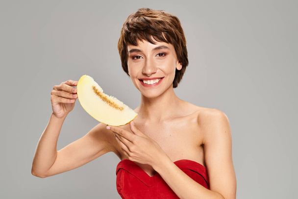 A young woman in a striking red dress posing with melon. - Photo, Image
