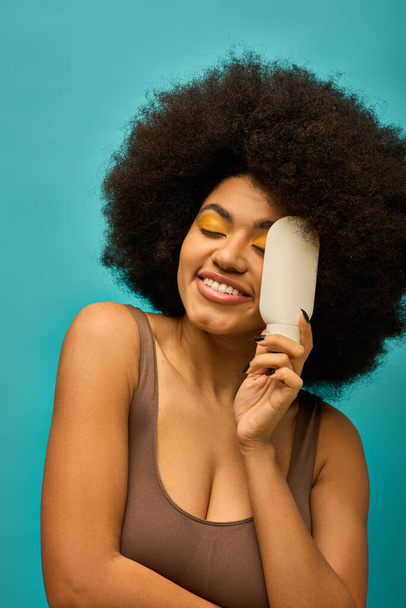 Femme afro-américaine élégante avec une tenue tendance tenant un pinceau sur son visage. - Photo, image