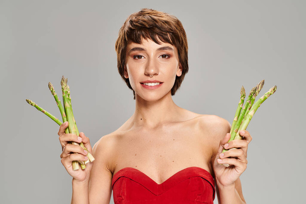 Stylish woman in red dress gracefully holding asparagus. - Photo, Image