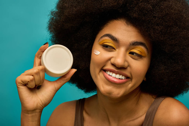 Elegante donna afro-americana con capelli ricci in possesso di un vaso di crema. - Foto, immagini