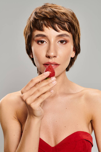 Mujer joven vestida de rojo comiendo delicadamente una fresa. - Foto, imagen