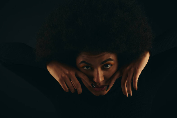 Μια κομψή Αφροαμερικανή με μοντέρνα ενδυμασία που καλύπτει το πρόσωπό της με τα χέρια της.. - Φωτογραφία, εικόνα