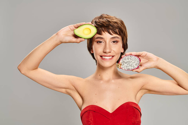 A woman radiates in a red dress while clutching a ripe avocado. - Photo, Image