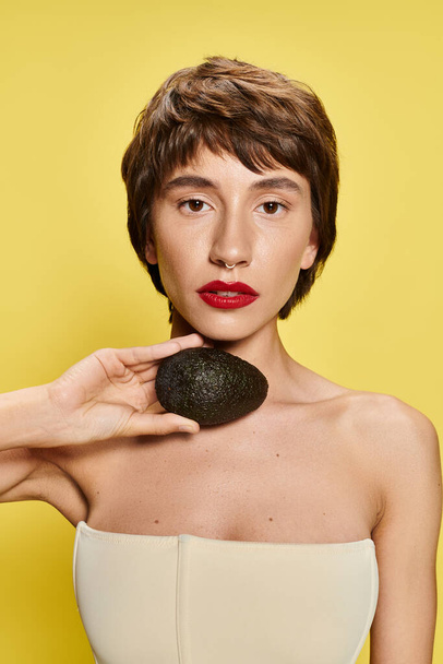 Женщина игриво держит авокадо перед лицом. - Фото, изображение