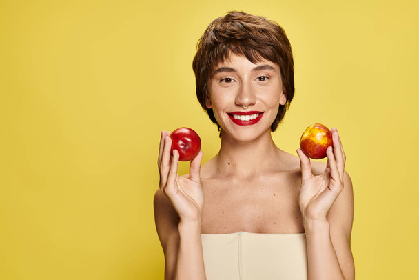A young woman holds two peaches with one in front of her face. - Photo, Image