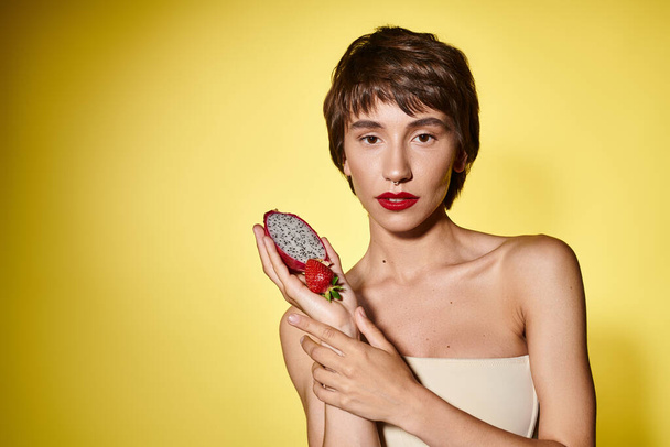 Egy fiatal nő kecsesen egy darab gyümölcsöt tart a kezében egy élénk háttérben.. - Fotó, kép